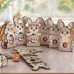 Pode incluir: Suportes de madeira em forma de coelho da Páscoa, cada um com um design único, para ovos Kinder Surpresa. Os coelhos têm vários acessórios, incluindo chapéus e coroas de flores. Alguns estão montados, outros embalados.