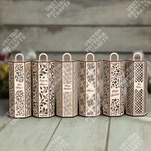 May include: Six wooden gift boxes with intricate laser-cut designs. Each box features a different pattern, including floral and geometric motifs. Some boxes have text that reads "Best Wishes!", "Enjoy the Moment!", "Happy Birthday!", "Cheers!", and "Happy Holidays!"