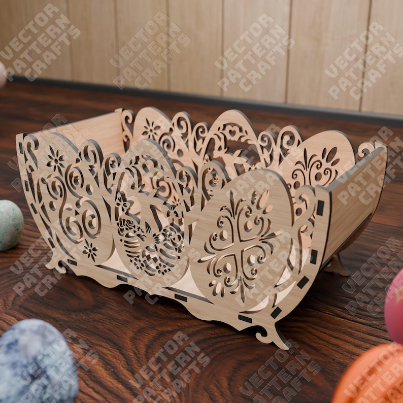May include: A light-colored wooden basket with intricate laser-cut designs. The basket features an egg-shaped design on the sides and floral patterns. The text "VECTOR PATTERN CRAFTS" is visible on the sides. The basket is on a wooden surface.