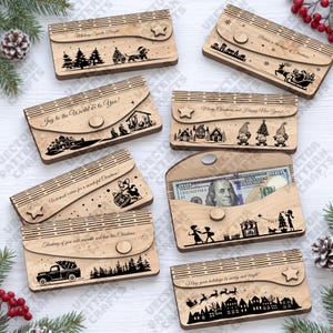 Könnte beinhalten: Eine Sammlung rechteckiger Geldgeschenkhüllen aus Holz mit lasergravierten Weihnachtsmotiven, Texten und Stern- oder Kreisverschlüssen. Eine Hülle ist geöffnet und zeigt einen darin liegenden Hundert-Dollar-Schein.