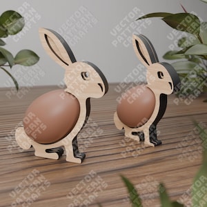 May include: Two wooden bunny egg holders. The bunnies are brown with black ears and stand on a wooden surface. Each bunny has a brown egg inside.