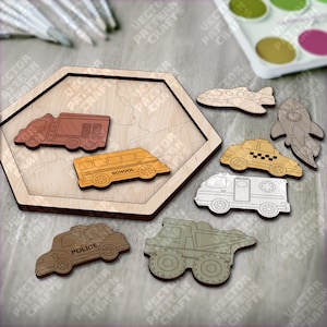 Könnte beinhalten: Holzpuzzle mit verschiedenen Fahrzeugen: Feuerwehrauto, Schulbus, Polizeiauto, Taxi, Krankenwagen, Muldenkipper, Flugzeug und Rakete. Die Puzzleteile sind in natürlichen Holztönen gehalten und liegen auf einer sechseckigen Holzbasis. Das Wort "SCHOOL" ist auf dem Schulbus zu sehen.