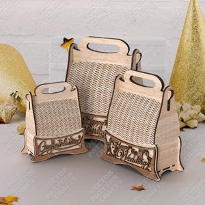 Può includere: Tre scatole regalo in legno con manici, con pannelli in stile tessuto e basi decorative. Le scatole sono incise con le frasi "Congratulazioni", "Buon Compleanno" e "Felice Matrimonio". Le scatole sono in legno chiaro.