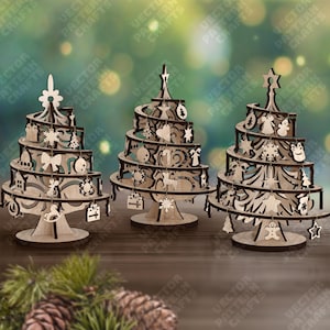 Peut inclure: Trois décorations de sapin de Noël en bois avec des motifs découpés complexes. Chaque arbre présente une structure en spirale avec des ornements décoratifs et un sommet en forme d'étoile ou de fleur. Les arbres sont exposés sur une surface en bois.