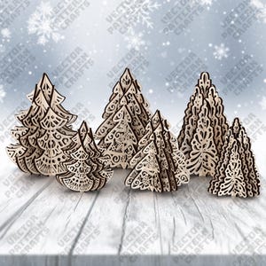 May include: A collection of laser-cut wooden Christmas trees with intricate designs. The trees vary in size and feature detailed patterns, with a light wood color and darker edges. They are arranged on a wooden surface with a snowy background.