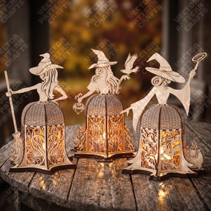 Può includere: Tre statuette di streghe in legno chiaro con cappelli a punta, ognuna dotata di una base cava a forma di lanterna con intricati disegni intagliati. Una tiene una scopa, un'altra una piccola zucca e un uccello, e la terza un lecca-lecca e un calderone.