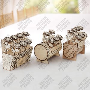 May include: Three wooden flower boxes with laser-cut floral designs. The boxes are in different shapes: a basket, a barrel, and a rectangular container. Each box holds wooden flowers, creating a decorative display. The boxes are made of light-colored wood.