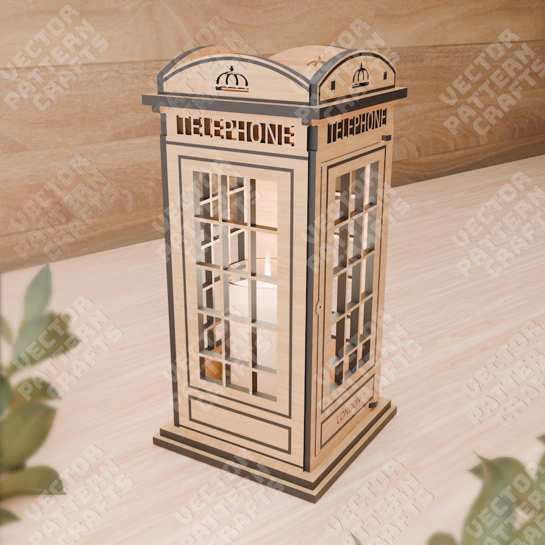 Pu&ograve; includere: Un modello in legno di una cabina telefonica rossa britannica con un portacandele all'interno. La cabina ha un tetto nero e un cartello che dice "Telefono" sul davanti. La base della cabina dice "Londra".