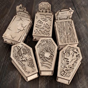 Könnte beinhalten: Eine Sammlung lasergeschnittener Holzkisten und Särge zum Thema Halloween. Die Kisten zeigen Designs wie ein Skelett, Spinnweben und den Text "Death by Chocolate". Die Särge haben aufwendige Ausschnitte und dekorative Elemente für Halloween.