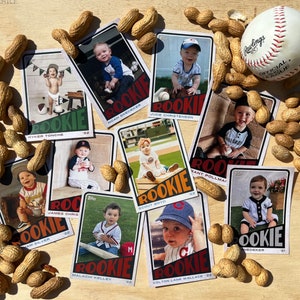 Peut inclure: Plusieurs cartes de baseball de recrues pour b&eacute;b&eacute;s, dispos&eacute;es sur une surface en bois avec des cacahu&egrave;tes et une balle de baseball. Chaque carte pr&eacute;sente une photo de b&eacute;b&eacute; et le mot "ROOKIE".