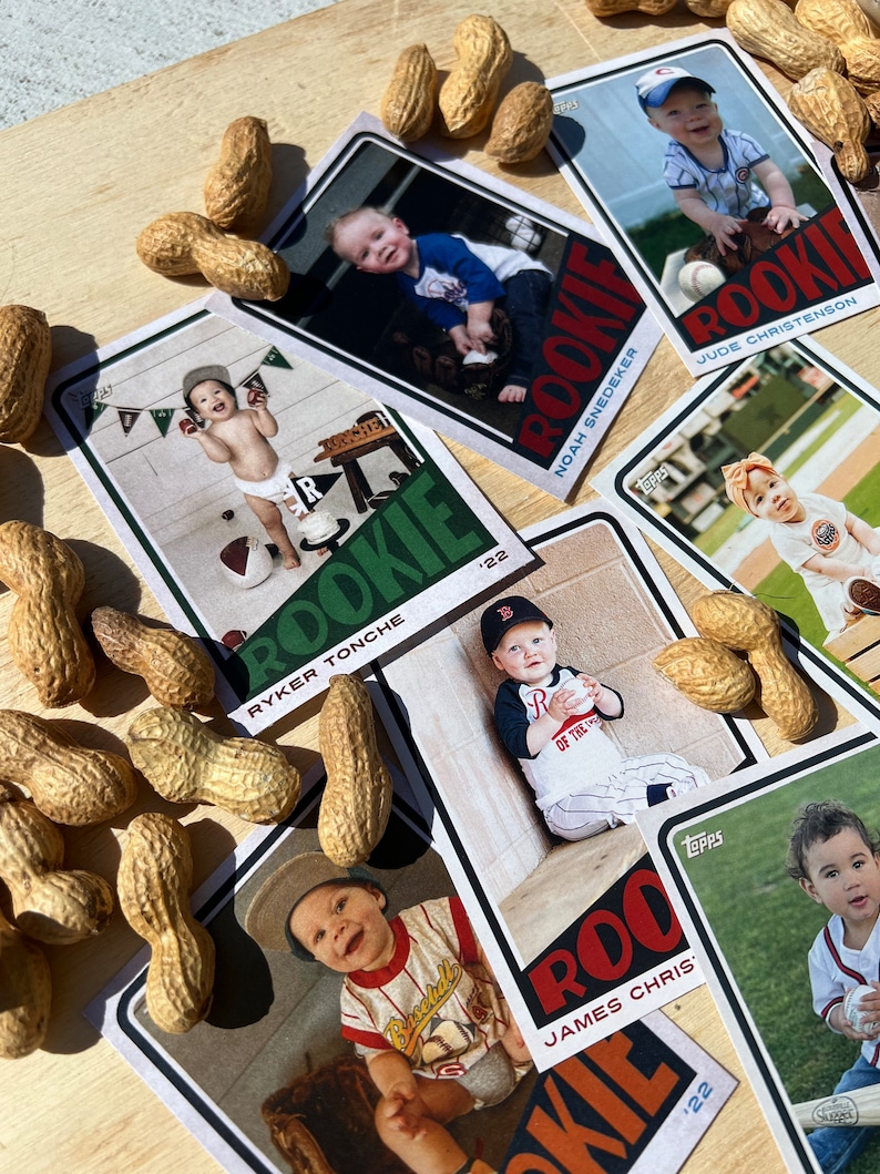 Peut inclure: Cartes de rookie de baseball pour b&eacute;b&eacute;s avec des photos d'enfants en tenues de baseball. Les cartes sont dispos&eacute;es sur une surface en bois, entour&eacute;es de cacahu&egrave;tes. On peut lire le mot "ROOKIE" et l'ann&eacute;e "'22".