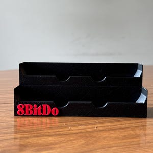May include: A black plastic organizer with two tiers and four compartments. The organizer has the text "8BitDo" printed in red on the front.