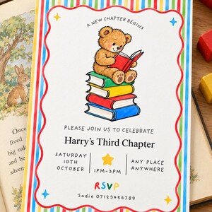 May include: A rectangular invitation card with a colorful vertical striped border and a scalloped red frame. It features a brown teddy bear reading a red book while sitting on a stack of green, yellow, red, and blue books. Text includes A NEW CHAPTER BEGINS, PLEASE JOIN US TO CELEBRATE, Harry's Third Chapter, SATURDAY 10TH OCTOBER, 1PM-3PM, ANY PLACE ANYWHERE, RSVP, and Sadie 07123456789.