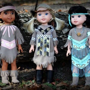 May include: Three dolls wearing Native American inspired outfits. The dolls are wearing grey dresses with fringe, beaded accents, and headbands. The dolls are standing in front of a tree trunk.