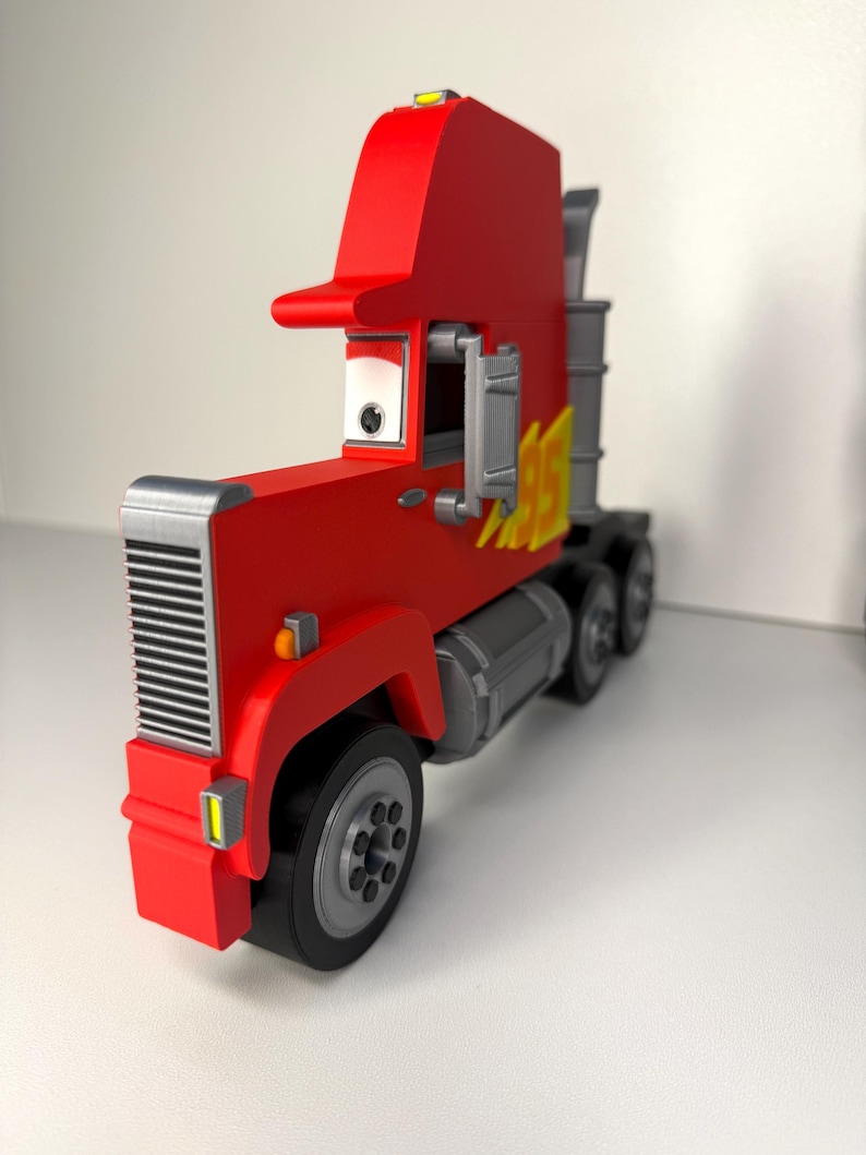 May include: A red toy semi-truck with a silver grill, wheels, and exhaust pipes. The truck has a tall cab and a yellow flame design on the side. The truck is a toy.