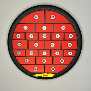 May include: A red and black advent calendar with 24 numbered compartments. The calendar is circular, with a black tire-like frame. The compartments are red with white numbers. The word "Bobble" is printed on a yellow lightning bolt.