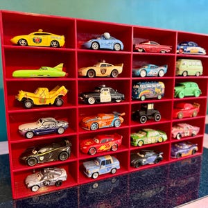 May include: A red display shelf filled with a collection of toy cars. The cars are various colors and styles, including a yellow taxi, a blue race car, and a green van. The shelf has multiple compartments.