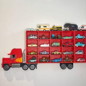 May include: A red truck-shaped shelf unit with multiple compartments, filled with various toy cars. The truck features a flame design on the side and is mounted on a white wall. The toy cars are of different colors and styles.