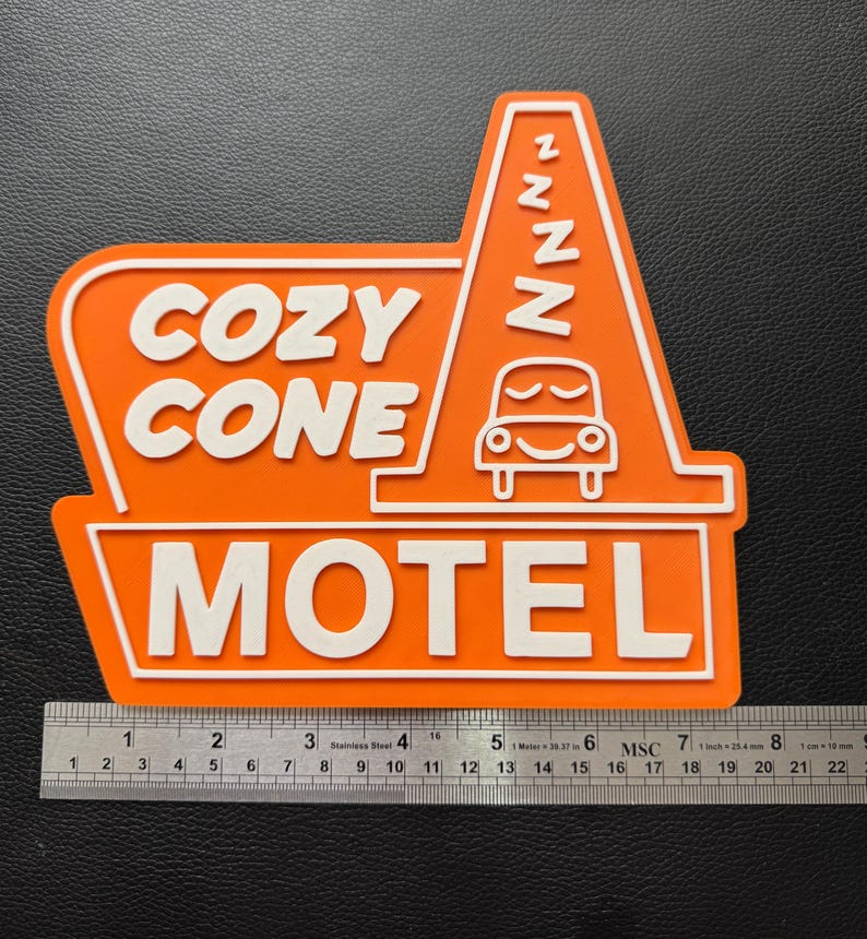 以下が含まれることがあります： オレンジと白の看板に「Cozy Cone Motel」の文字と、ZZZが書かれた漫画の車が描かれています。