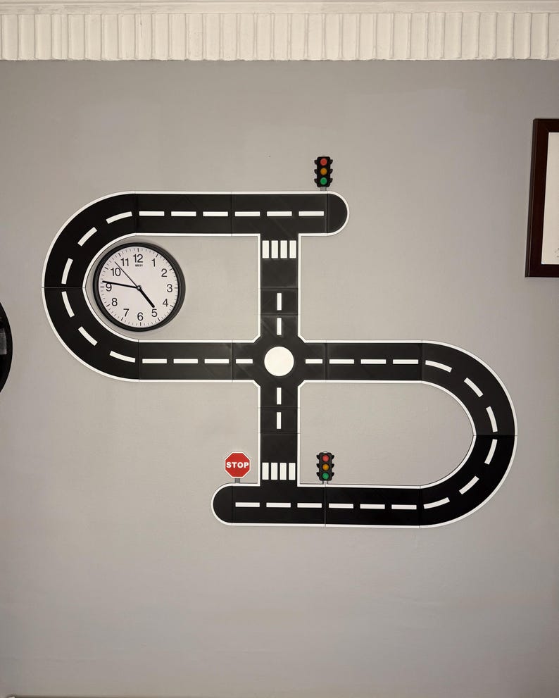 May include: A wall-mounted road play set with a clock, stop sign, and traffic lights. The black road pieces have white dashed lines and are arranged in a unique pattern. The clock has black hands and white numbers. The stop sign is red and white.