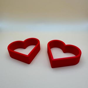 Pair of red 3D-printed heart-shaped place card holders, perfect for weddings and romantic events. these holders can be customised in your choice of colours to match your theme, making them ideal for unique table décor and personalised celebrations.