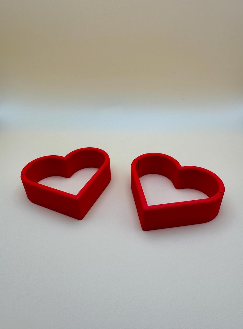 Pair of red 3D-printed heart-shaped place card holders, perfect for weddings and romantic events. these holders can be customised in your choice of colours to match your theme, making them ideal for unique table décor and personalised celebrations.