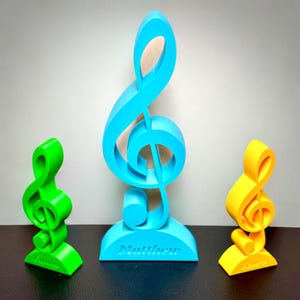 Personalised treble clef trophies in blue, green, and yellow, each featuring a custom name. A perfect music gift for musicians, teachers, or students, ideal for display on a desk, shelf, or piano. Available in multiple sizes and colours.