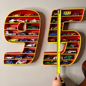 May include: Red and yellow number-shaped shelves, filled with toy cars. The shelves are in the shape of the numbers 9 and 5. The height of the 95 shelves is measured with a tape measure, approximately 30 inches.