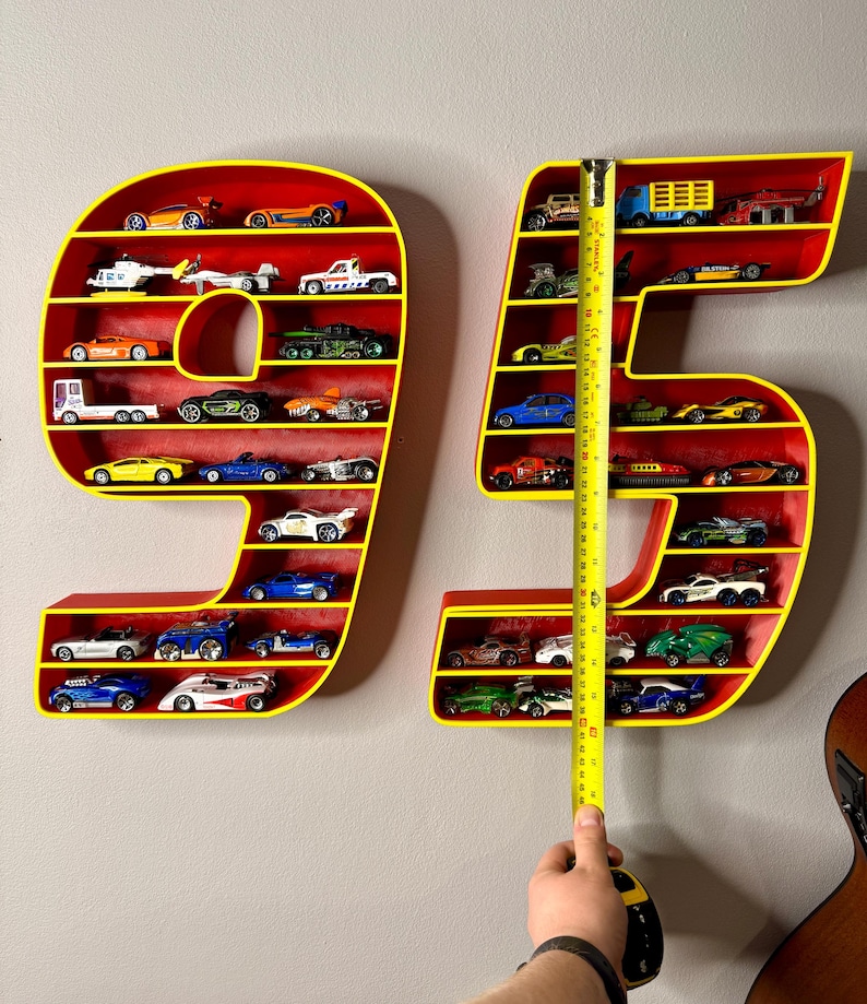 May include: Red and yellow number-shaped shelves, filled with toy cars. The shelves are in the shape of the numbers 9 and 5. The height of the 95 shelves is measured with a tape measure, approximately 30 inches.