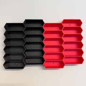 May include: A wall-mounted storage organizer featuring a modular honeycomb pattern. The unit consists of two distinct sections: one side is matte black and the other is bright red. Each section contains multiple hexagonal compartments for storage.