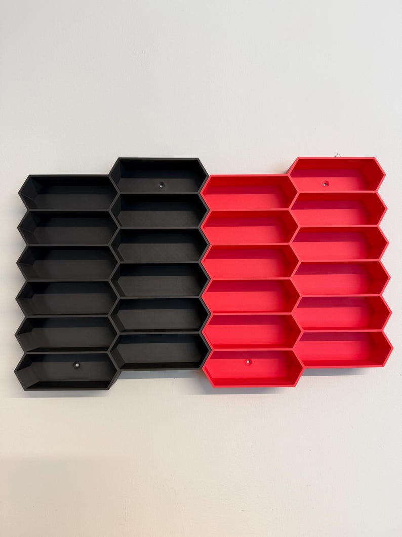 May include: A wall-mounted storage organizer featuring a modular honeycomb pattern. The unit consists of two distinct sections: one side is matte black and the other is bright red. Each section contains multiple hexagonal compartments for storage.