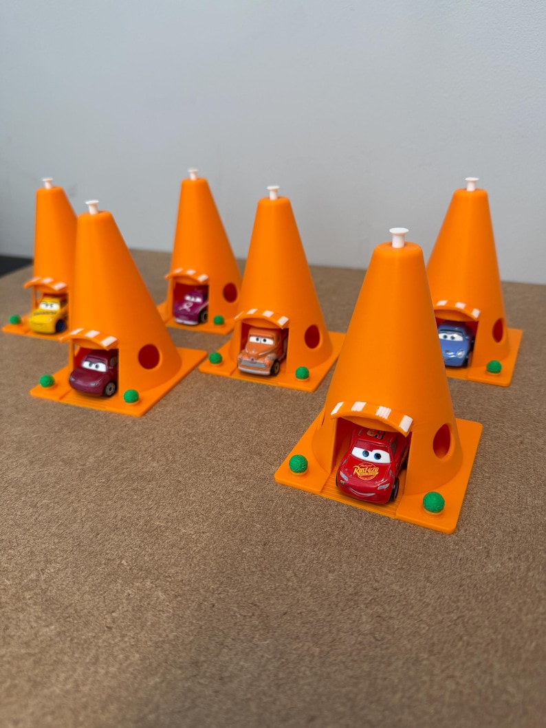 May include: A collection of orange traffic cone-shaped toy structures, each with a small car inside. The cars are various colors, including red, yellow, purple, and blue. The structures have a white top and are set on a square base.