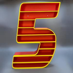 May include: A large, number-shaped shelf unit in the form of the number 5. The shelves are red with yellow trim. The unit is designed to be mounted on a wall and has pre-drilled holes for hanging. The overall design is modern and eye-catching.