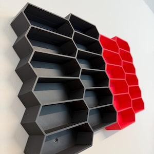 May include: A wall-mounted storage unit featuring a series of interconnected hexagonal compartments. The majority of the structure is matte dark gray, while a smaller section on the right side is a vibrant, solid red. The unit has an open-front design.