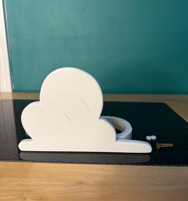 May include: A white cloud-shaped shelf with curved details, likely for decorative purposes. Includes small screws for mounting. The shelf is on a black surface with a teal background.