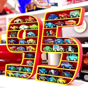 May include: A red and yellow display shelf shaped like the number 95, filled with miniature toy cars. The shelf has multiple compartments holding various colorful toy vehicles. The background includes a sign that says "Cars" and other toy cars.