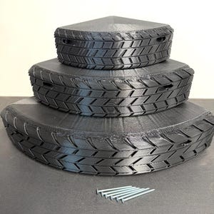 May include: Three-tiered black storage containers with a tire tread design. The containers are triangular and stackable, with a set of silver screws nearby. The containers are made of a matte black material.
