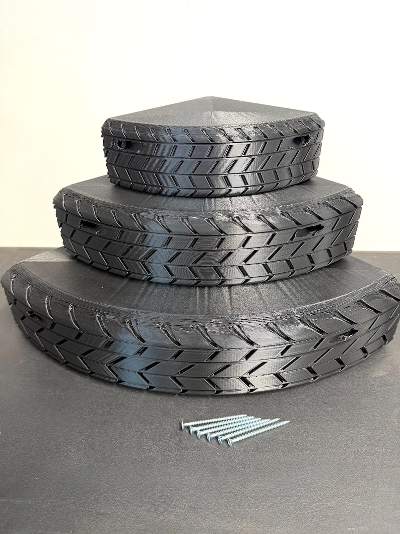 May include: Three-tiered black storage containers with a tire tread design. The containers are triangular and stackable, with a set of silver screws nearby. The containers are made of a matte black material.