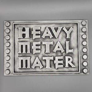 Peut inclure: Panneau rectangulaire argent&eacute; avec les mots "HEAVY METAL MATER" en lettres en relief. Le panneau a une surface textur&eacute;e et une bordure avec des accents circulaires. Le fond est gris uni.