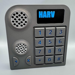 May include: A gray, rectangular device with a keypad, speakers, and the word "HARV" in blue. The keypad has blue numbers and symbols. The device has a retro, futuristic design.