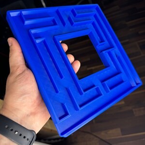 A 3D-printed, decorative light switch cover with a maze-like design. The intricate pattern adds a unique and playful touch to any room, making it both functional and visually appealing for various settings.