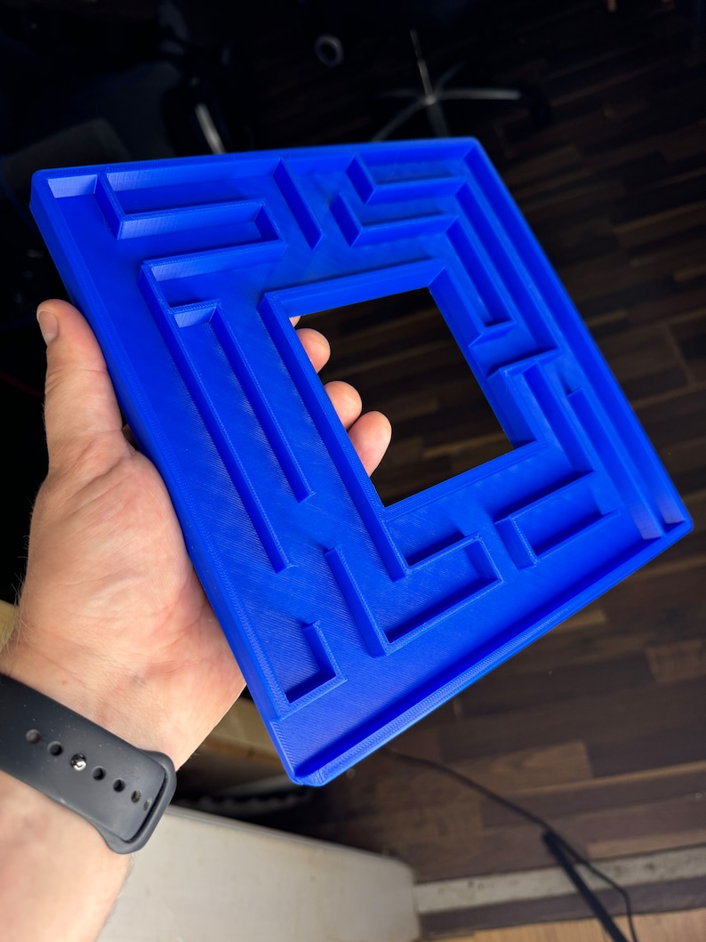 A 3D-printed, decorative light switch cover with a maze-like design. The intricate pattern adds a unique and playful touch to any room, making it both functional and visually appealing for various settings.