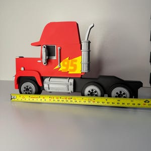 May include: A red and black toy truck with the number 95 and a yellow flame design on the side. The truck has a silver exhaust pipe and wheels. The truck measures approximately 12 inches in length.
