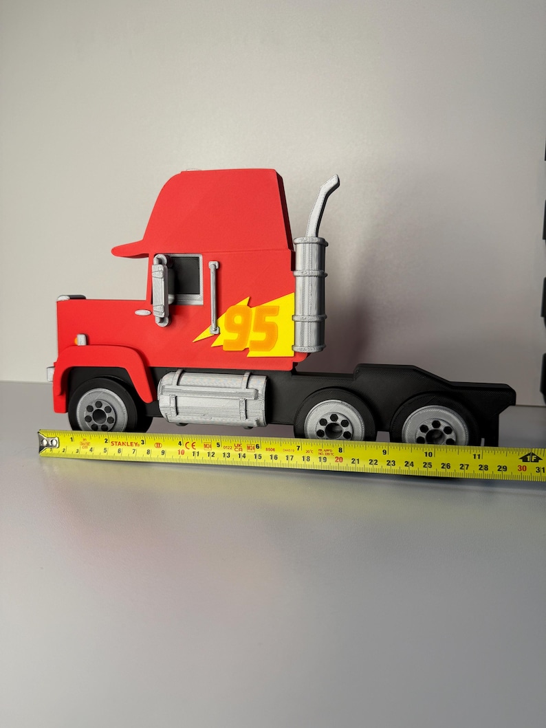 May include: A red and black toy truck with the number 95 and a yellow flame design on the side. The truck has a silver exhaust pipe and wheels. The truck measures approximately 12 inches in length.