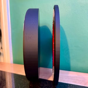 May include: A black, circular object with a red and white design on the side. The object is standing upright on a dark surface, with a green and blue background.