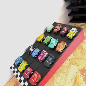 May include: A display of colorful toy race cars arranged on a black track with a red border. The cars are various colors, including red, yellow, blue, and green. A checkered flag design is at the end of the track.