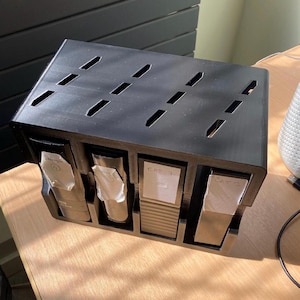 May include: A black, rectangular organizer with four compartments. Each compartment holds a white packet. The top of the organizer has several angled slits. The labels read "CAT 3" and "CAT 1".