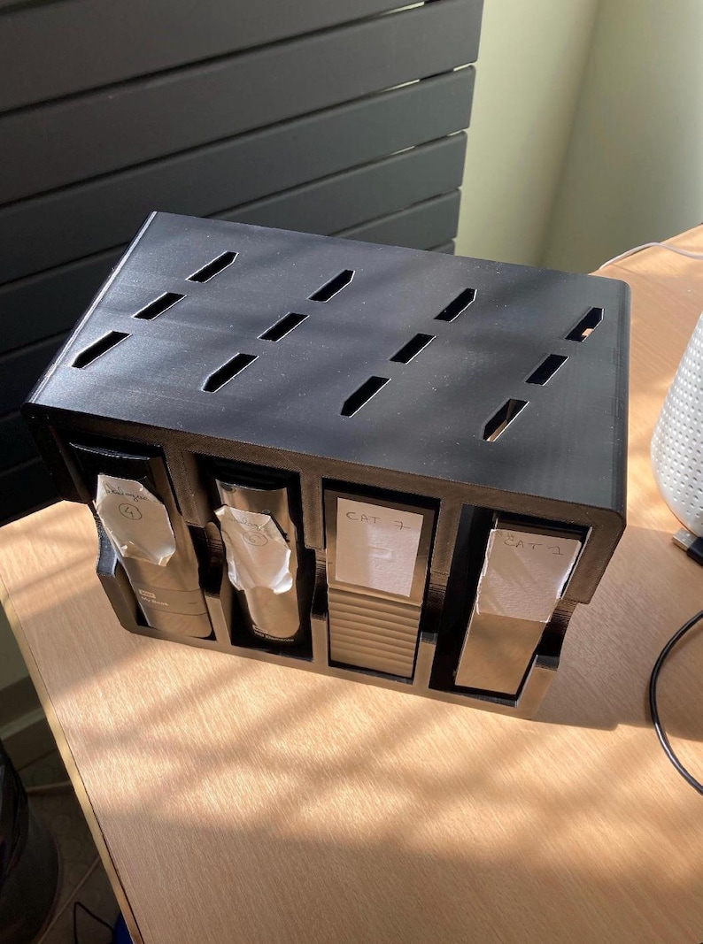 May include: A black, rectangular organizer with four compartments. Each compartment holds a white packet. The top of the organizer has several angled slits. The labels read "CAT 3" and "CAT 1".