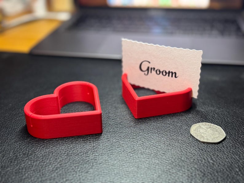 Red 3D-printed heart-shaped place card holders displayed with a “Groom” card and a coin for size comparison. Ideal for weddings, receptions, and bridal showers, these durable holders combine practicality and style.