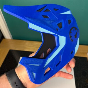 May include: A blue and light blue full-face helmet with a visor. The helmet has a speedometer graphic on the side and several ventilation holes. The interior is black. The helmet is held by a person.